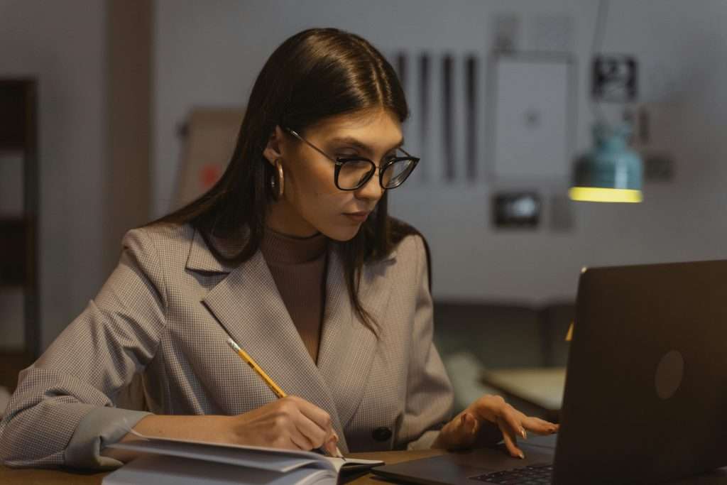 Confident businesswoman working on laptop and taking notes in office setting.